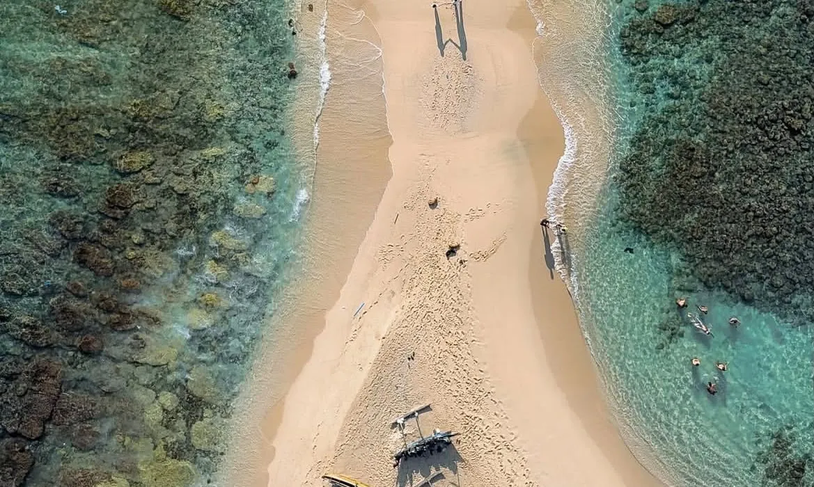 Snorkellers in the clear water beside the sandbar at Blue Beach Island, seen from above