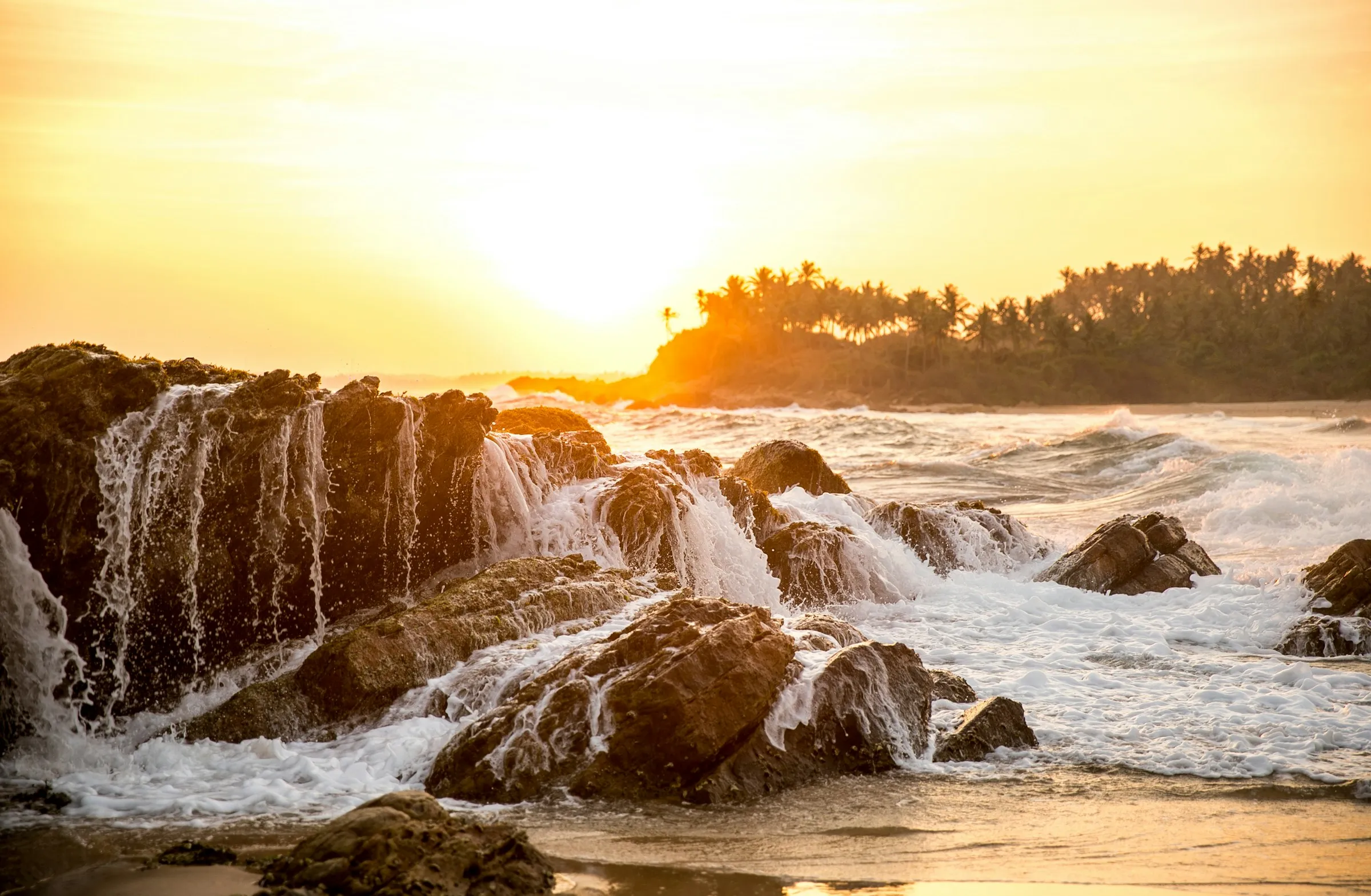 Waves washing over the rocks at Dickwella Beach in golden evening light